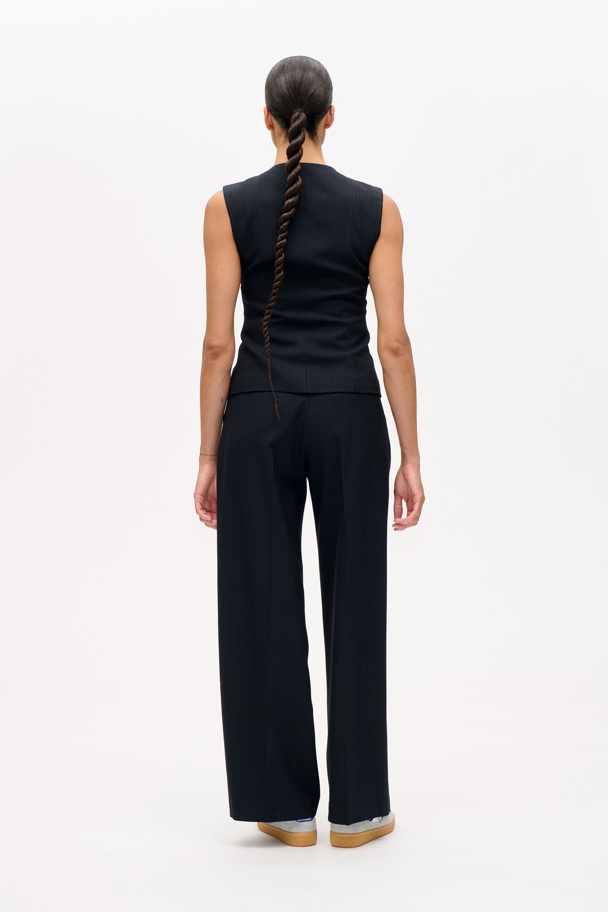 Achteraanzicht van een model in een donkere, fijn krijtgestreepte mouwloze top en een bijpassende broek met wijde pijpen.