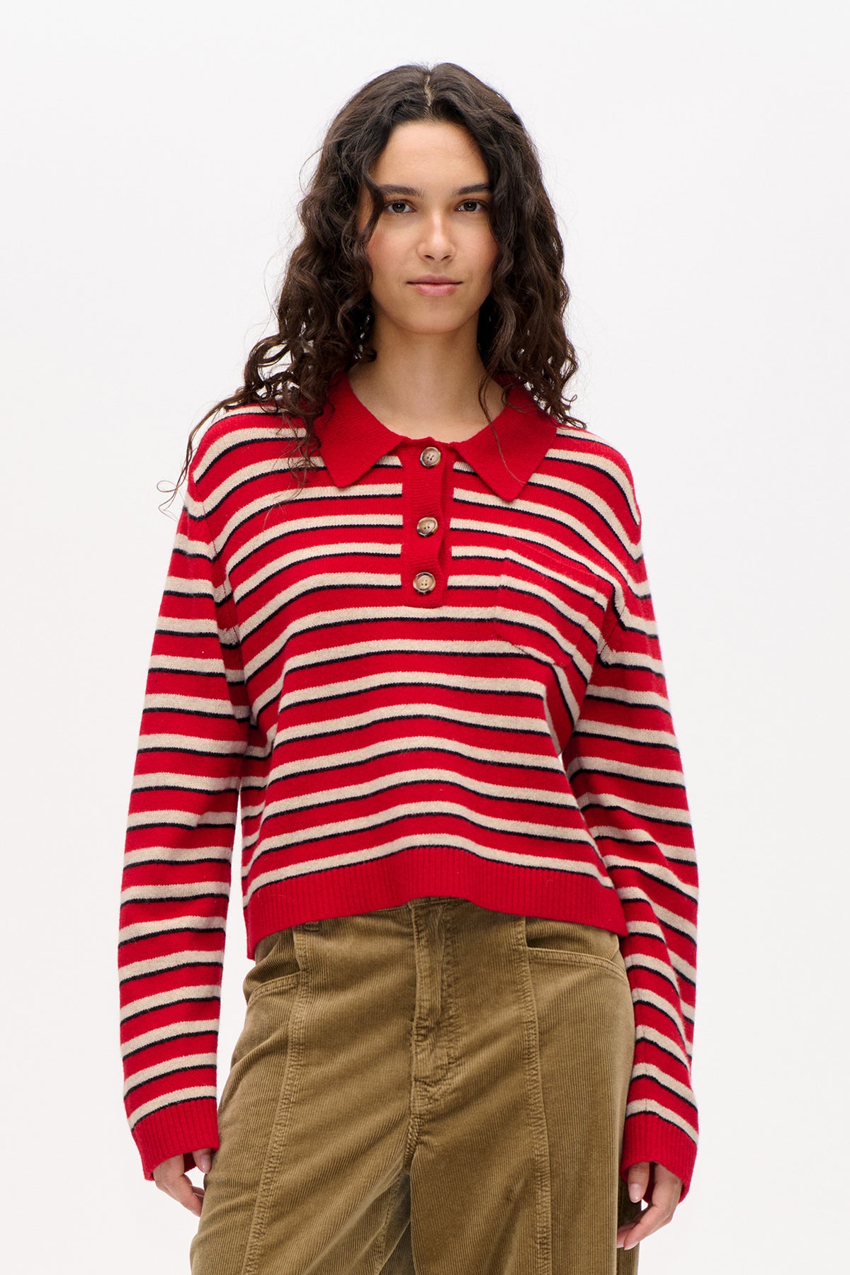 Front view of a model wearing a red knit long-sleeved collared top with cream and dark navy stripes and brown corduroy trousers