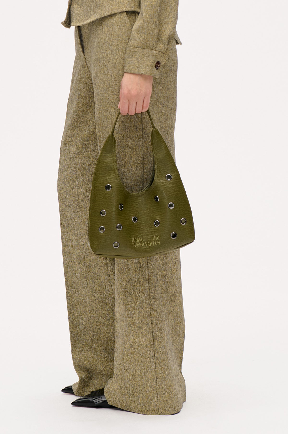 Olive-green tote with metal eyelets and Baum und Pferdgarten logo, carried beside a brown-olive textured suit.