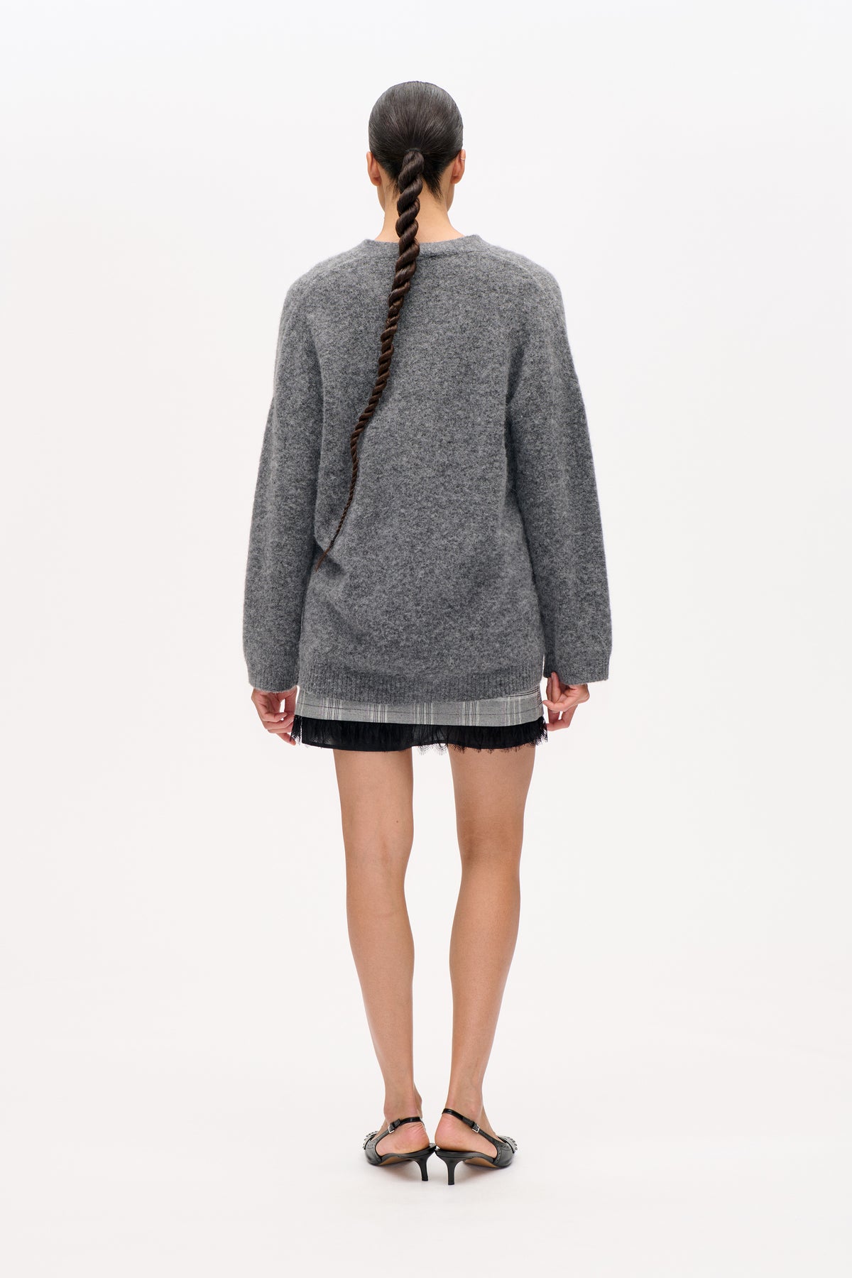 Rear view of a model in an oversized mottled grey sweater over a plaid mini skirt with a black lace hem.