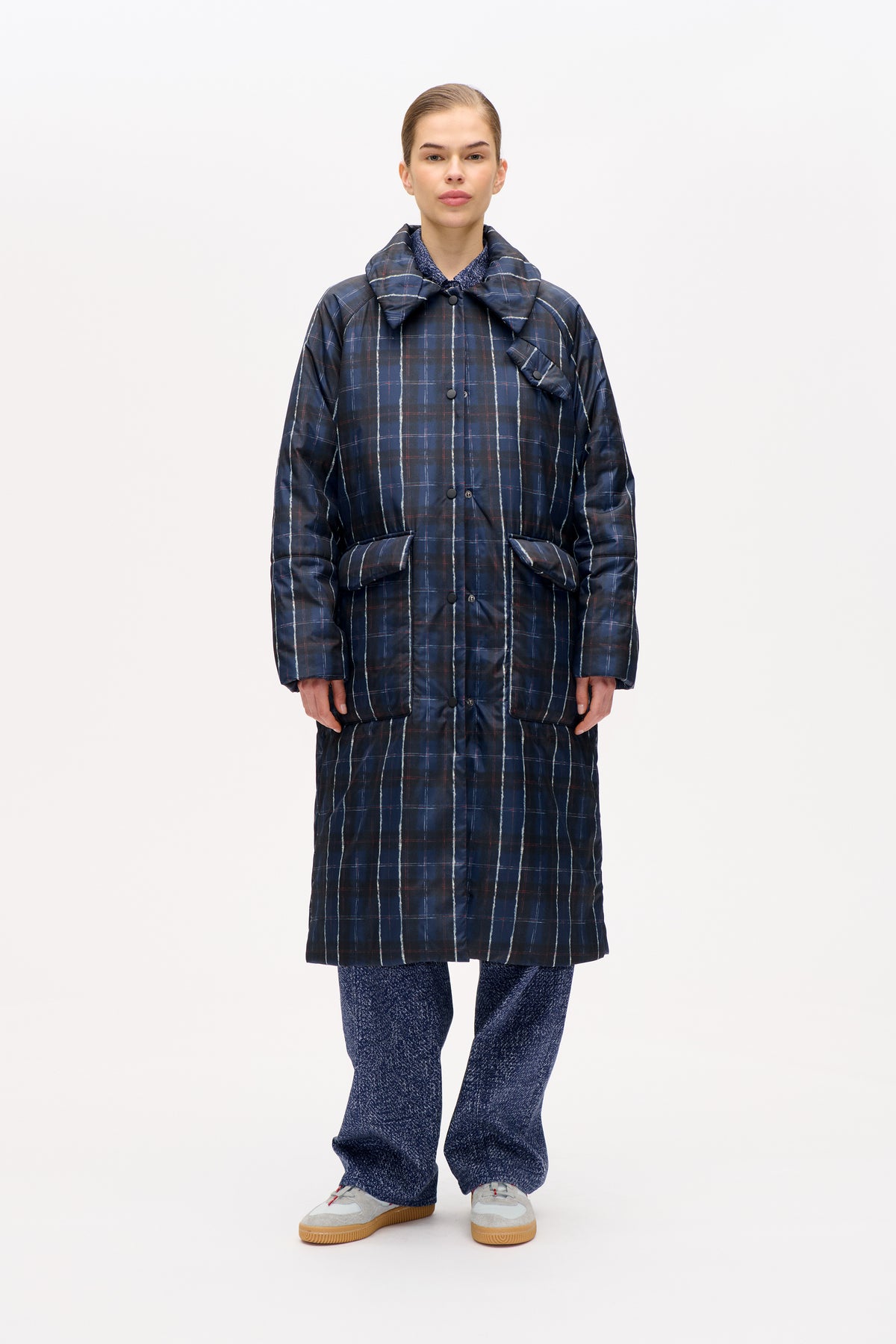 Front view of a long navy padded coat with a large collar, button closure and white and red windowpane checks.