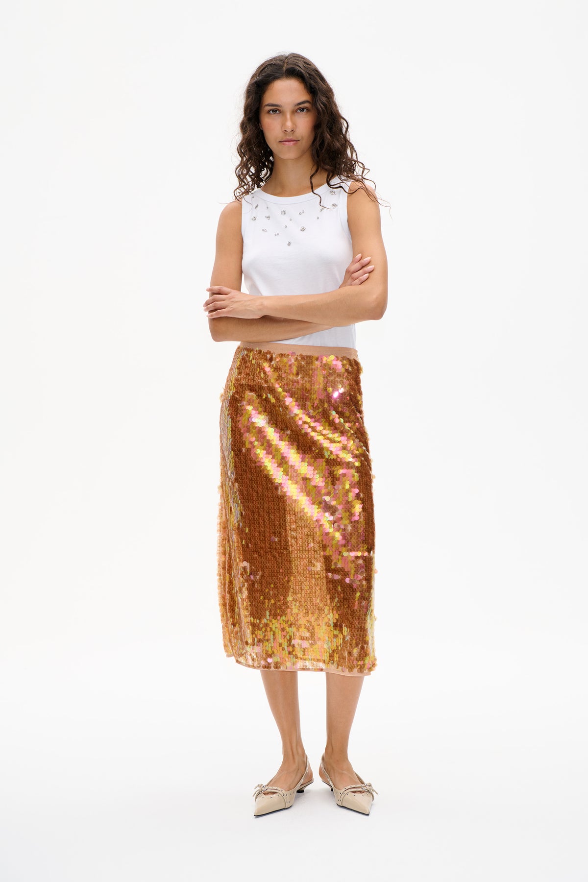 Model wearing a white sleeveless top with scattered embellishments and a knee-length skirt covered in iridescent gold and pink sequins, front view.