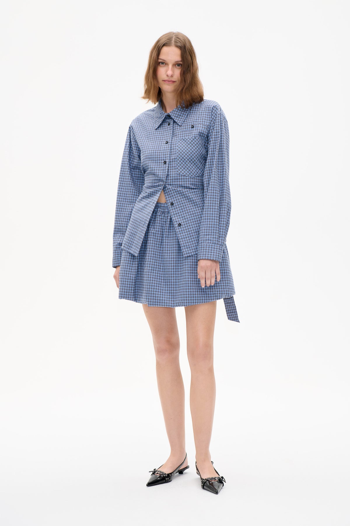Model wearing a blue checked button-front shirt with a chest pocket and a matching pleated skirt.