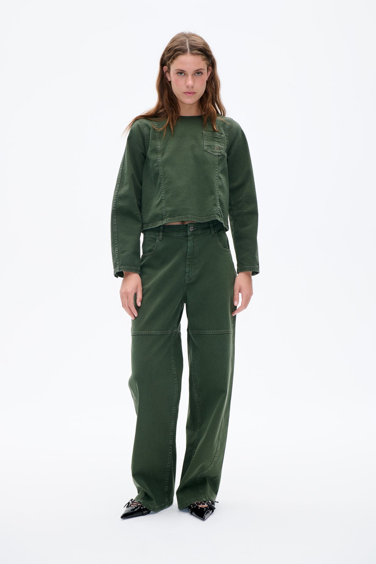 Front-facing model wears a washed dark-green long-sleeved top with a chest pocket and matching wide-leg trousers.