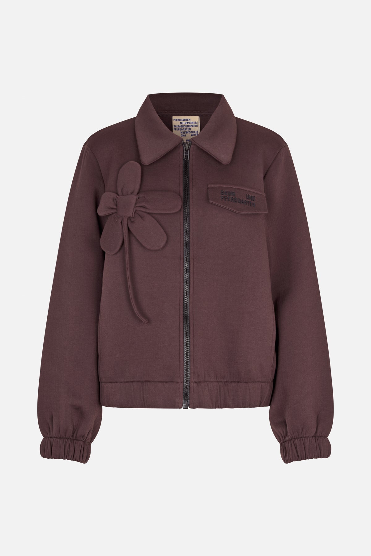 Front view of a plum zip-front jacket with a pointed collar, elasticated cuffs and hem, a fabric flower appliqué and chest patch.