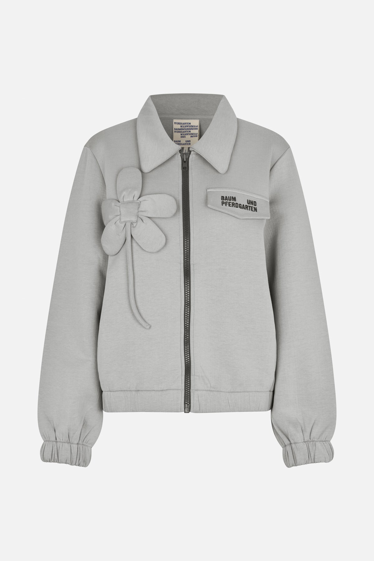 Front view of a light grey zip-up jacket with a pointed collar, gathered cuffs, a flower appliqué and a logo flap pocket.