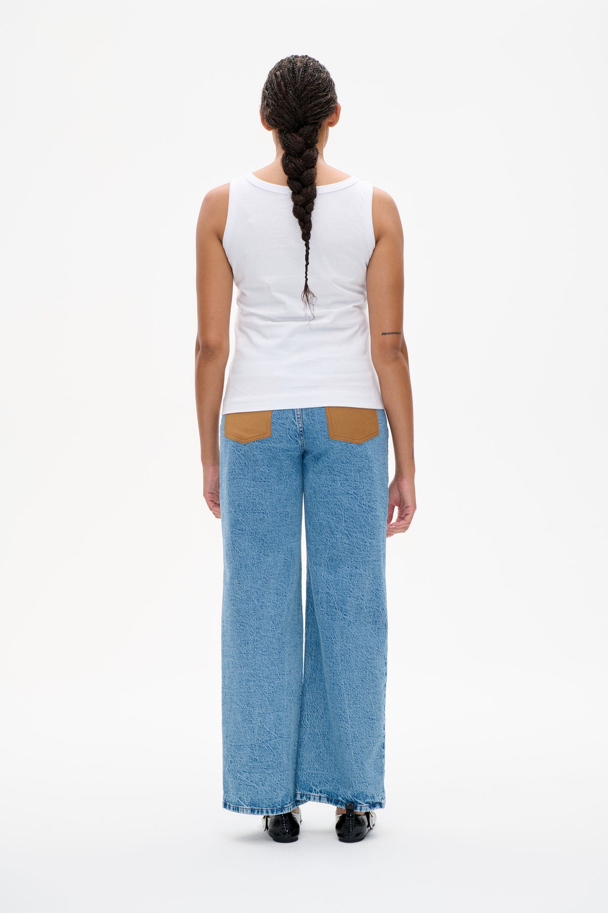 Back view of a model wearing a white sleeveless top and wide-leg blue jeans with tan back pockets.
