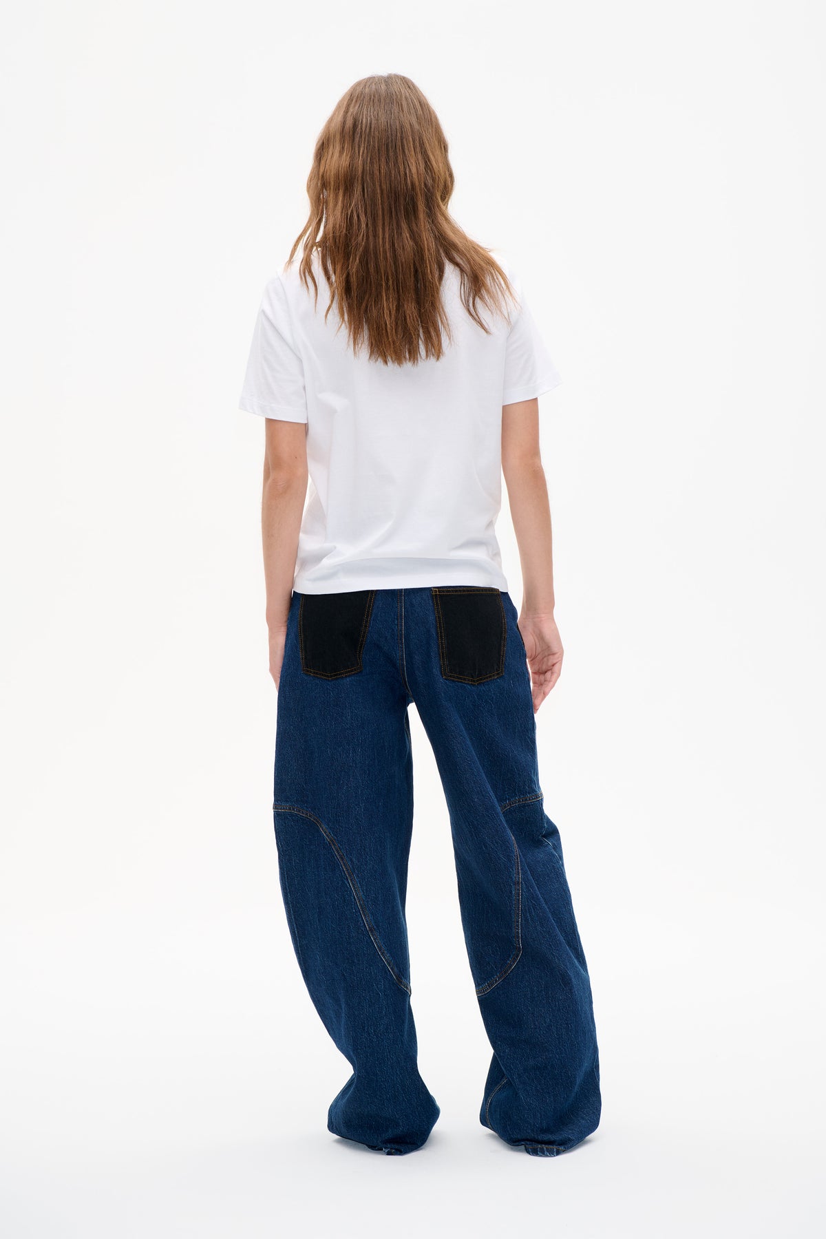 Achteraanzicht van een donkerblauwe wijdvallende jeans met zwarte opgestikte zakken en gebogen naden met contrasterende stiksels, gedragen met een eenvoudig wit T-shirt.