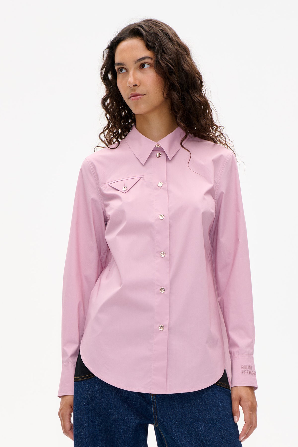 Front view of a model wearing a pale pink button-up shirt with a pointed collar, decorative buttons and a flap chest pocket, paired with dark jeans.