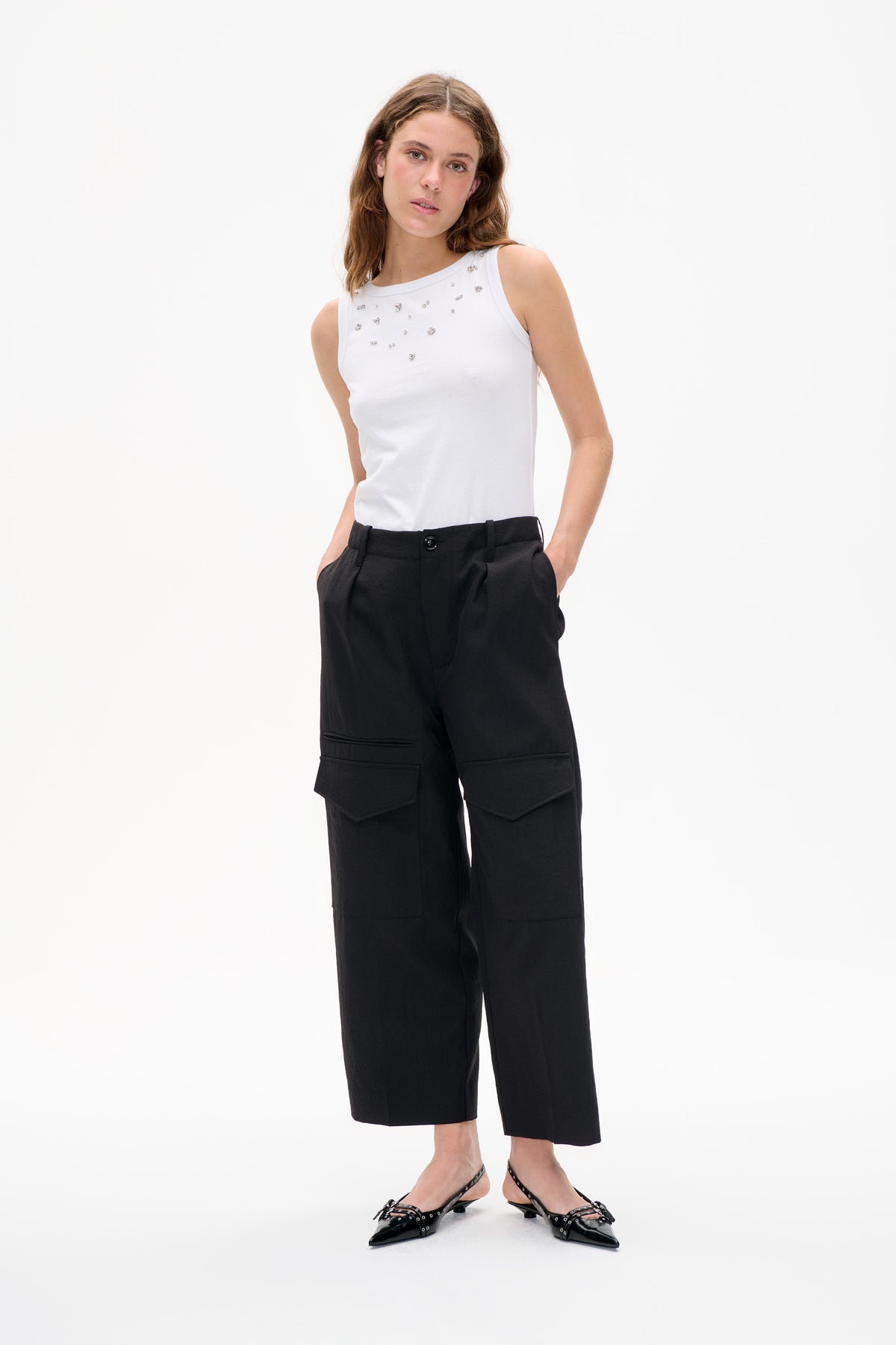 Model wearing a white sleeveless top with scattered silver embellishments and black cropped wide-leg trousers with large patch pockets.