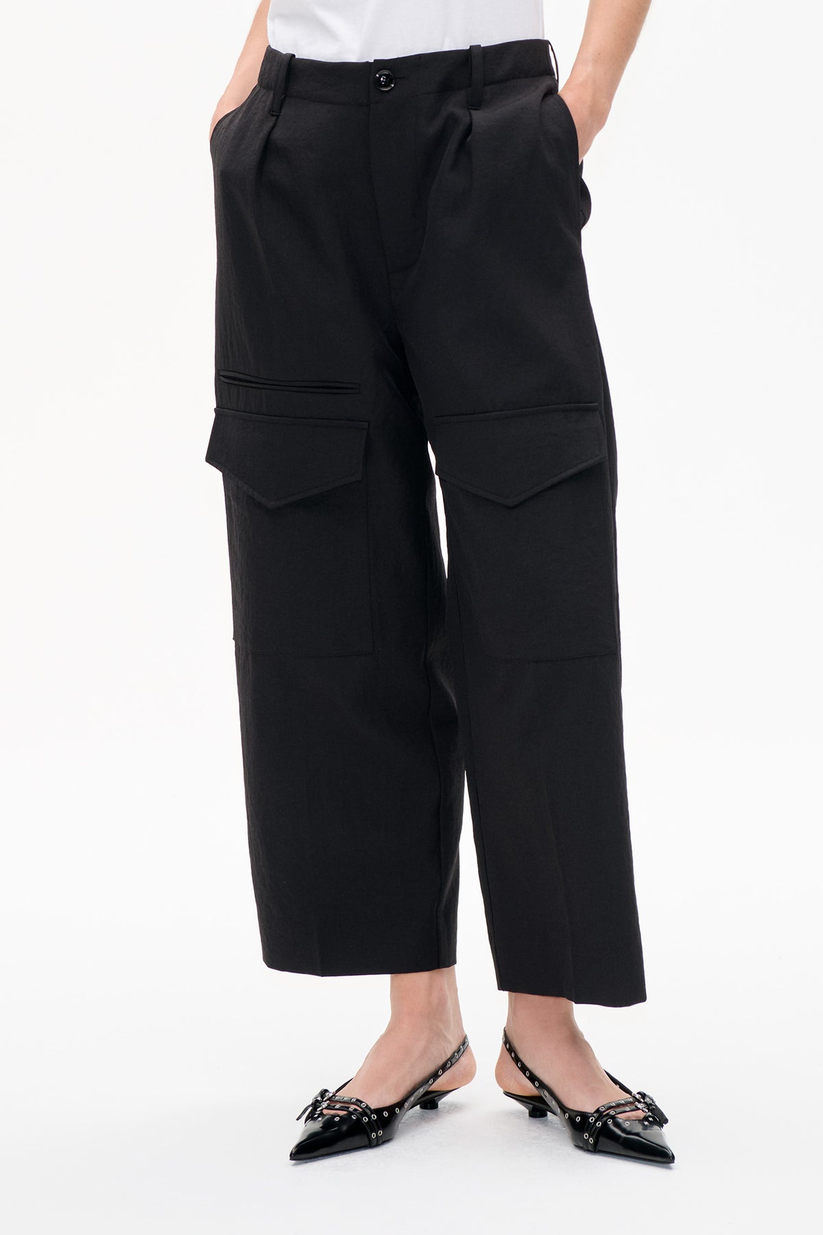 Front detail of black tailored knee-length shorts with a buttoned waist, pleats and large flap pockets.
