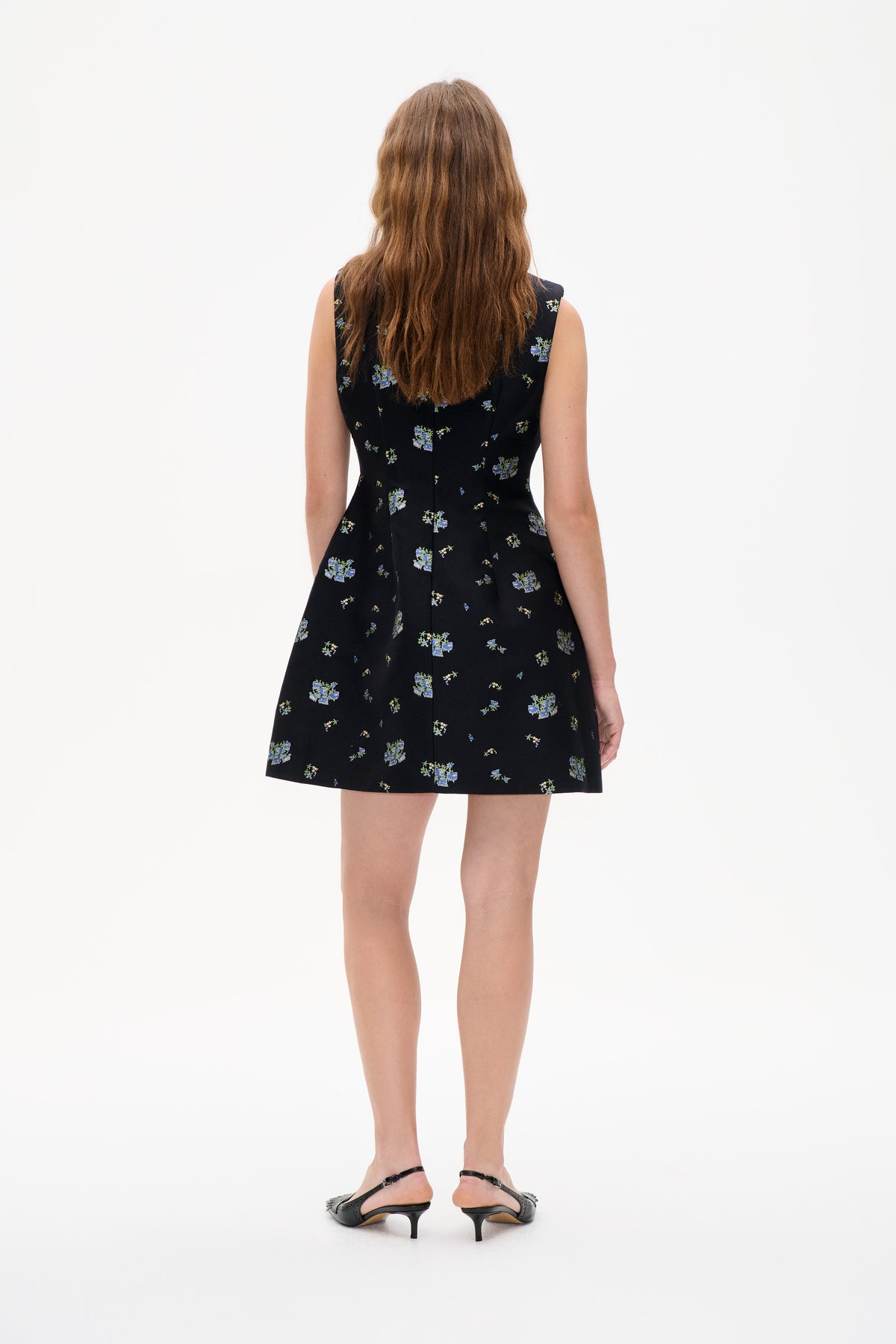 Achteraanzicht van een mouwloze zwarte aansluitende mini-jurk met verspreide blauwe en groene bloemenprint.