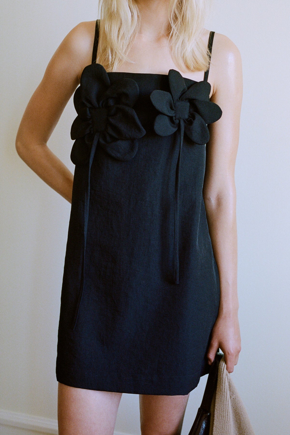Close-up of a model wearing a black sleeveless dress with oversized layered fabric flower appliqués across the front.