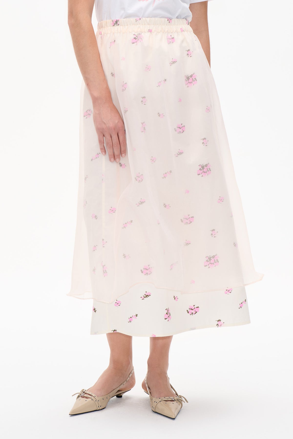 Front detail of a sheer ivory midi skirt with an elastic waist and scattered pink floral print, layered over a matching skirt.