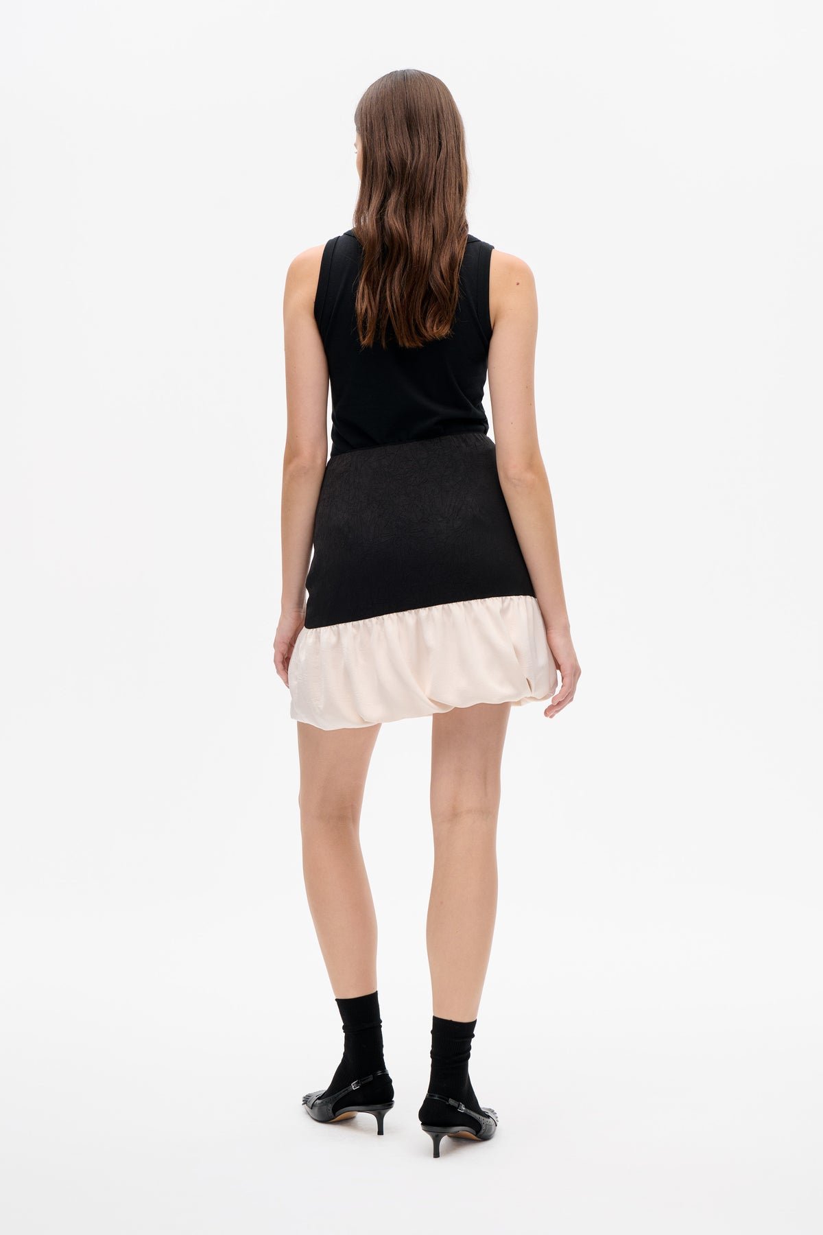 Back view of a model wearing a black sleeveless top and a black textured skirt with a gathered ivory bubble hem.