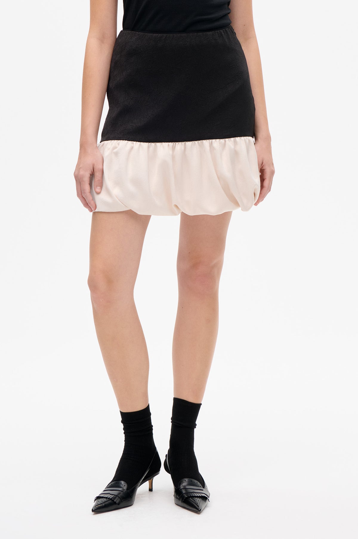 Front detail of a black textured mini skirt with a gathered ivory bubble hem, worn with a black top.