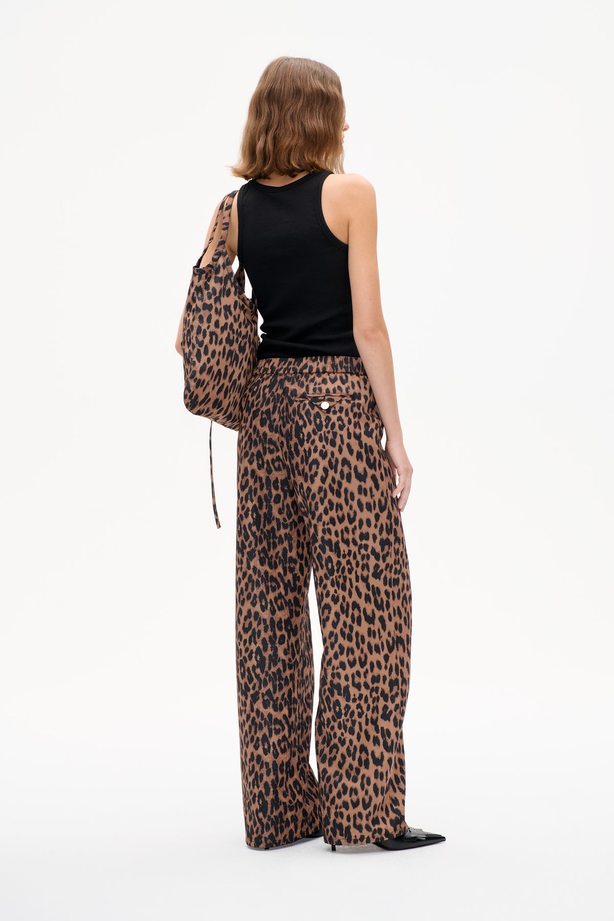 Model von hinten in schwarzem, ärmellosem Top und weit geschnittenen Hosen mit braun-schwarzem Leopardenprint, dazu eine passende Schultertasche.