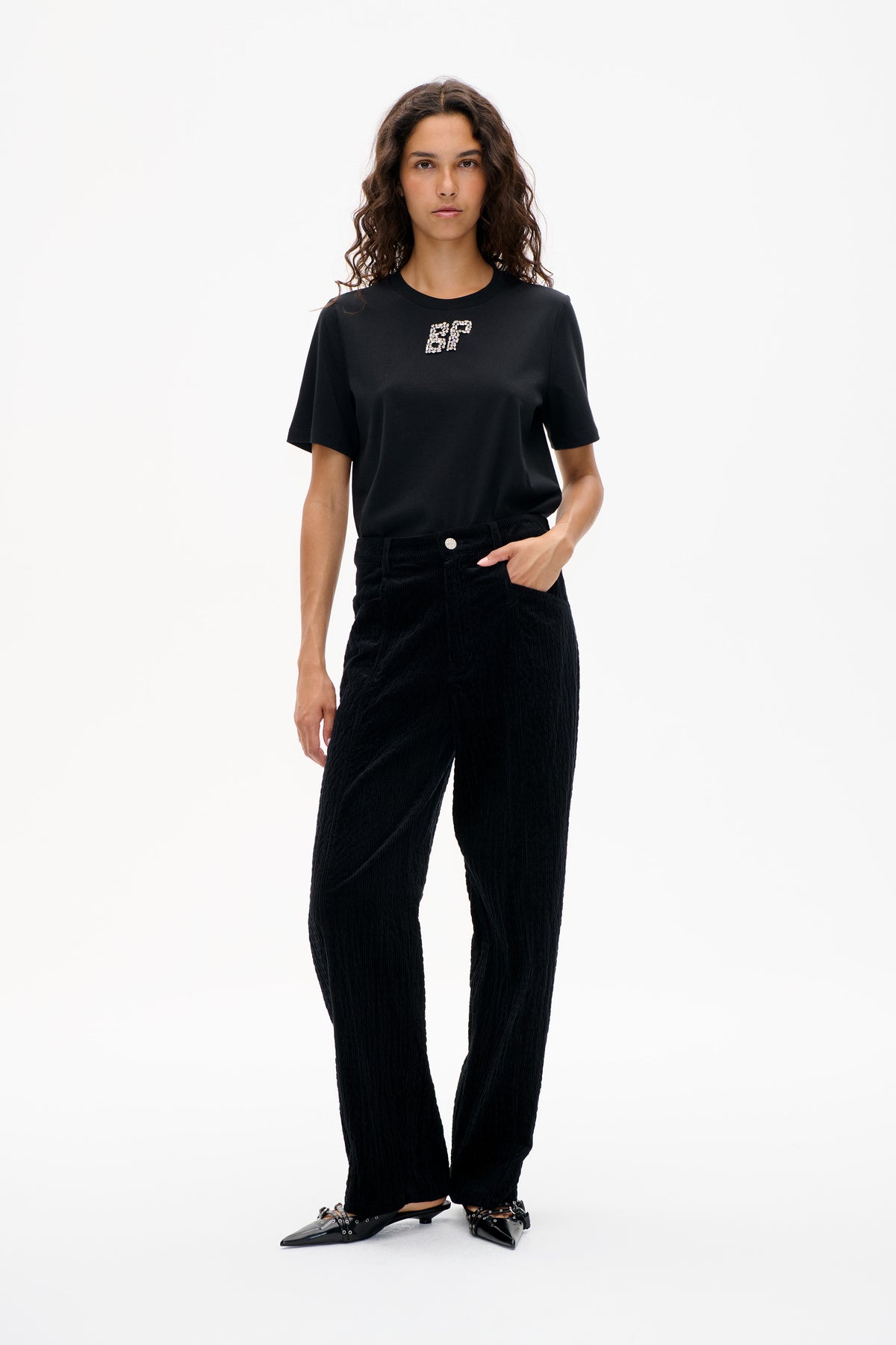 Front view of a model wearing a black short-sleeved T-shirt with a jeweled chest motif and black corduroy trousers.