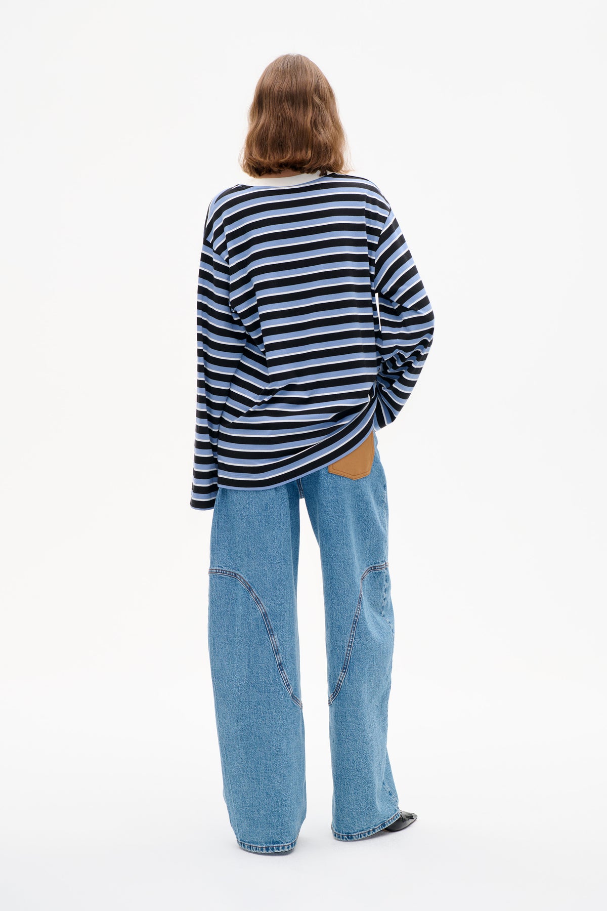 Back view of a model wearing a black, light blue and white striped long-sleeved top with wide-leg blue jeans.