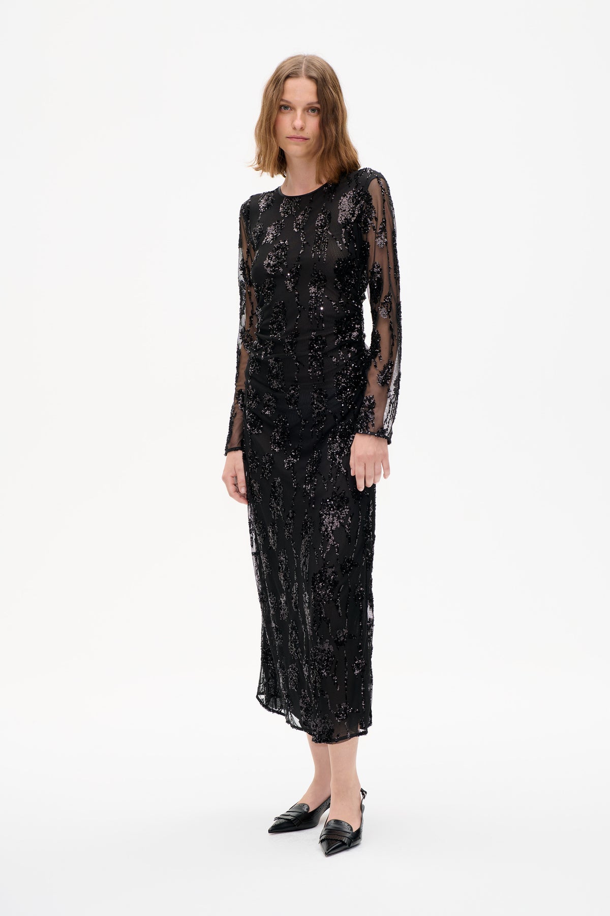 Model wearing a black sheer long-sleeved midi dress with scattered sequin embellishments, shown from the front against a white background.