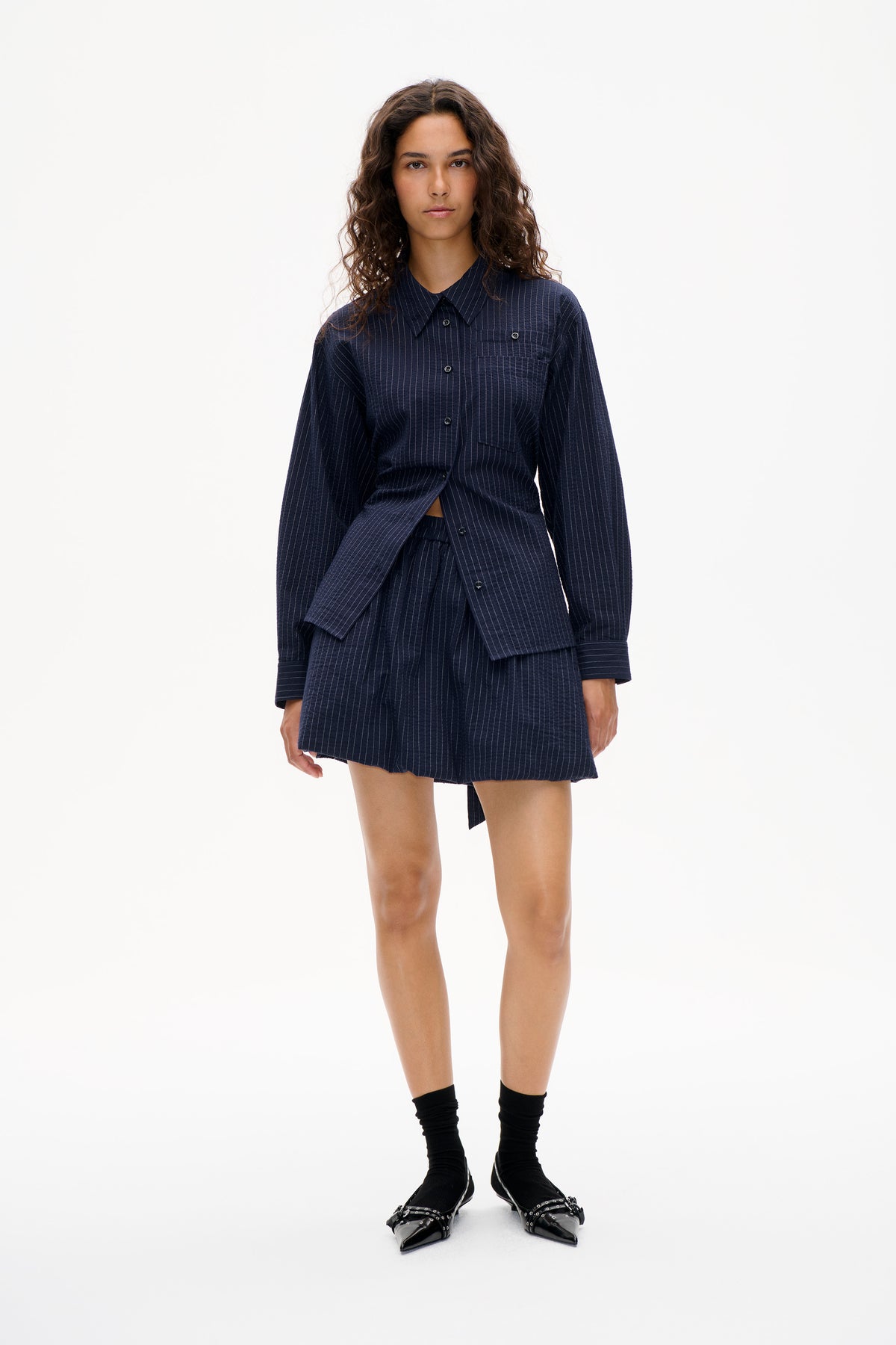 Model trägt ein marineblaues Nadelstreifenhemd mit durchgehender Knopfleiste, Brusttaschen und passenden Shorts, von vorne gezeigt.