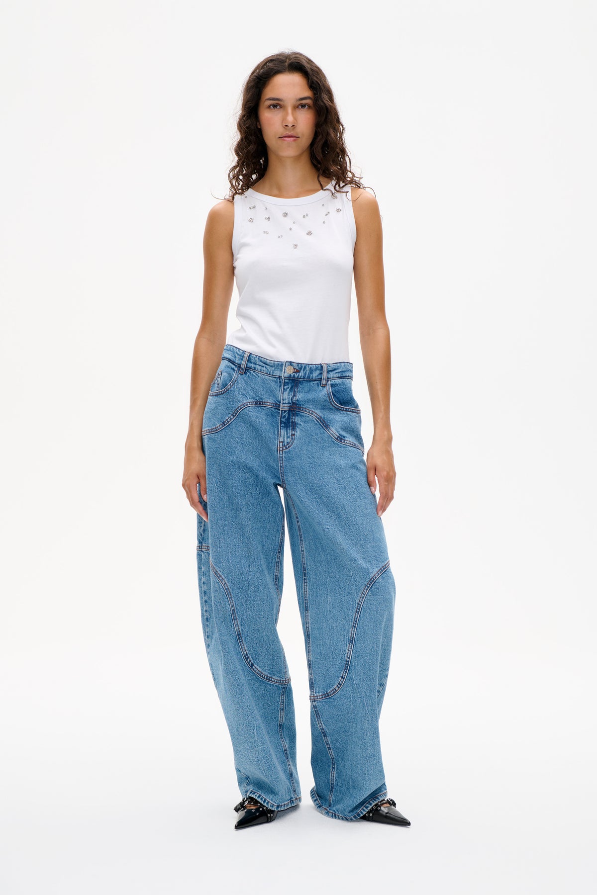 Vorderansicht eines weißen, ärmellosen Tops mit verstreuten, funkelnden Verzierungen, kombiniert mit hellblauen, weit geschnittenen Jeans.