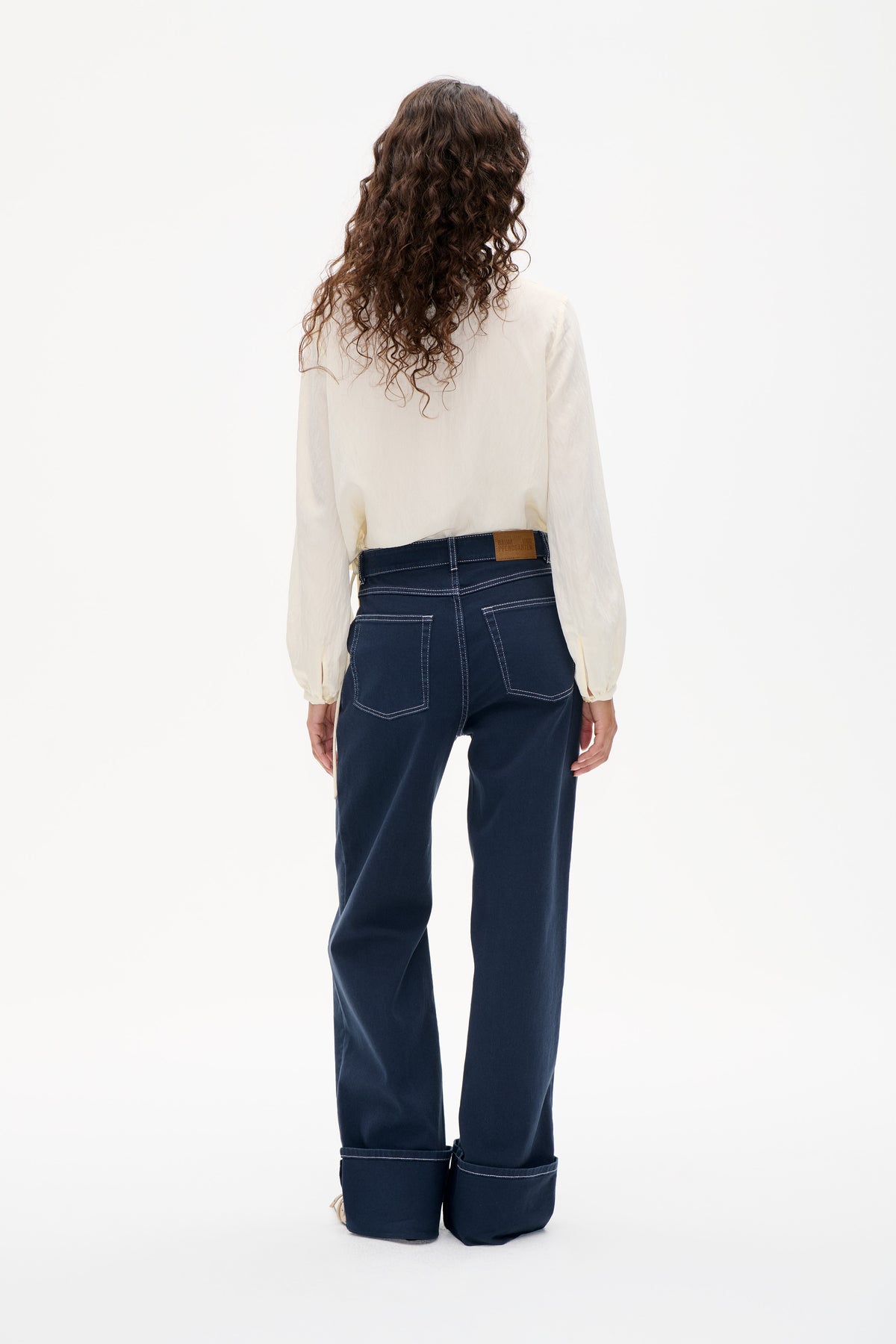 Rückansicht dunkler Indigo-Jeans mit weitem Bein, kontrastierenden Nähten und übergroßen aufgekrempelten Säumen, kombiniert mit einer elfenbeinfarbenen Langarmbluse.
