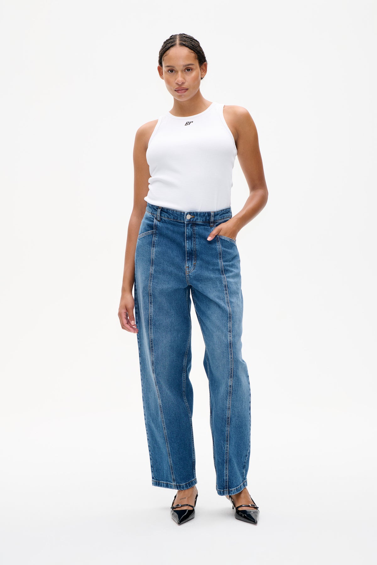 Model wearing a white sleeveless ribbed top with a small chest logo and blue wide-leg jeans, shown from the front.