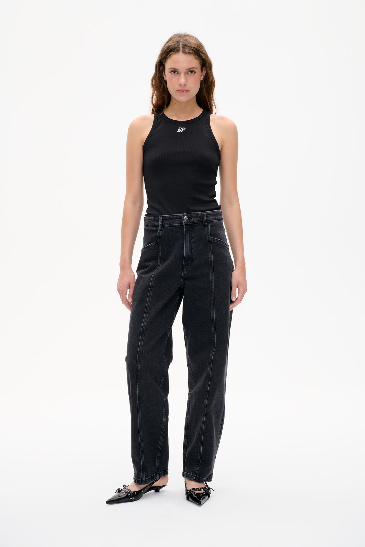 Front view of a model wearing a black ribbed sleeveless top with a small white chest logo and charcoal washed jeans.
