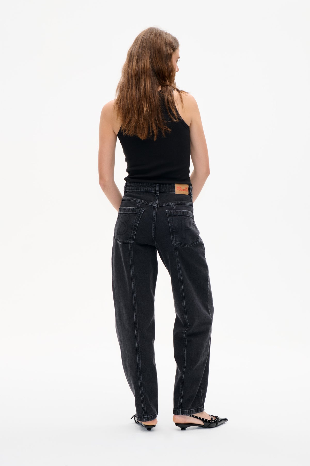 Back view of a model wearing a black sleeveless top and dark charcoal washed jeans with back pockets and wide legs.