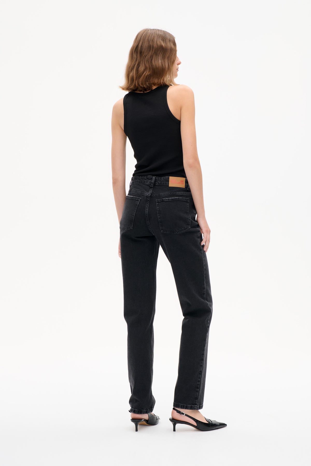 Back view of a model wearing a black sleeveless top and dark-wash straight-leg jeans with two rear patch pockets.