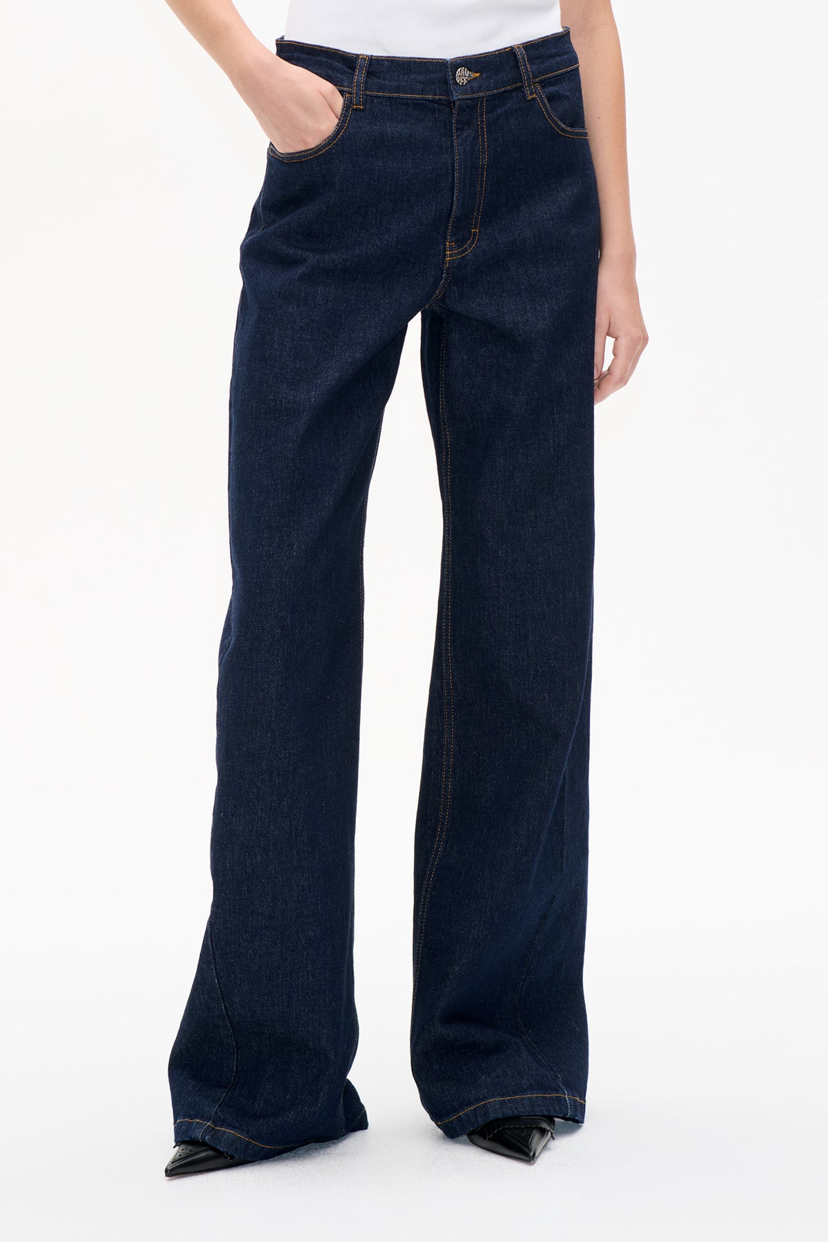 Front detail of dark indigo wide-leg jeans with contrast stitching, belt loops, button closure and curved front pockets.