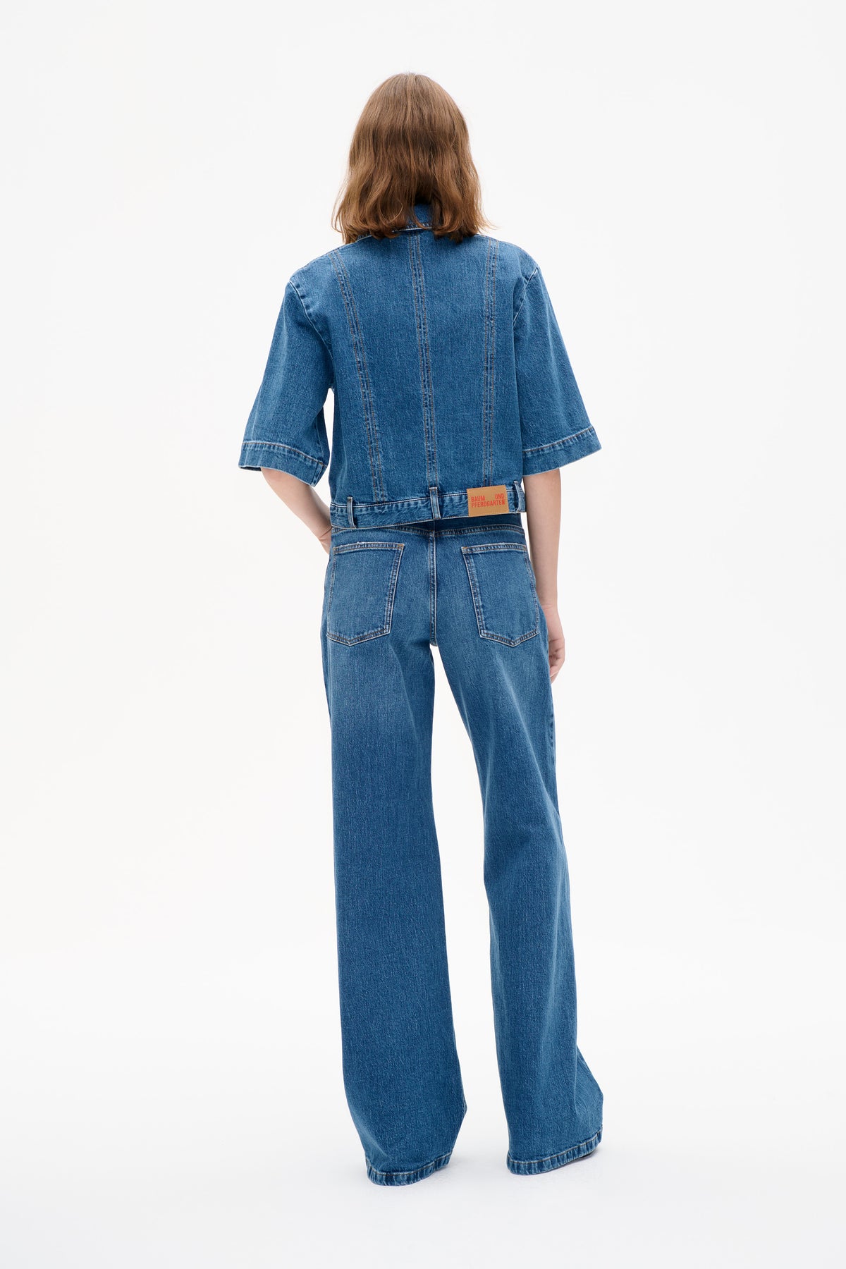 Back view of a model wearing a blue denim jacket with wide short sleeves and matching wide-leg jeans.