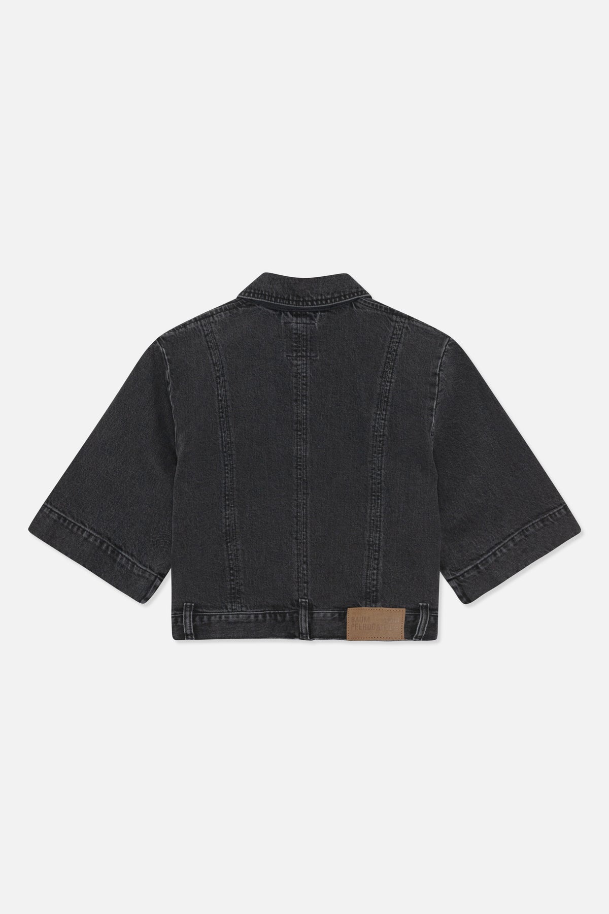 Back view of a dark washed-black denim jacket with a pointed collar, wide sleeves, panel seams and a brown logo patch at the hem.
