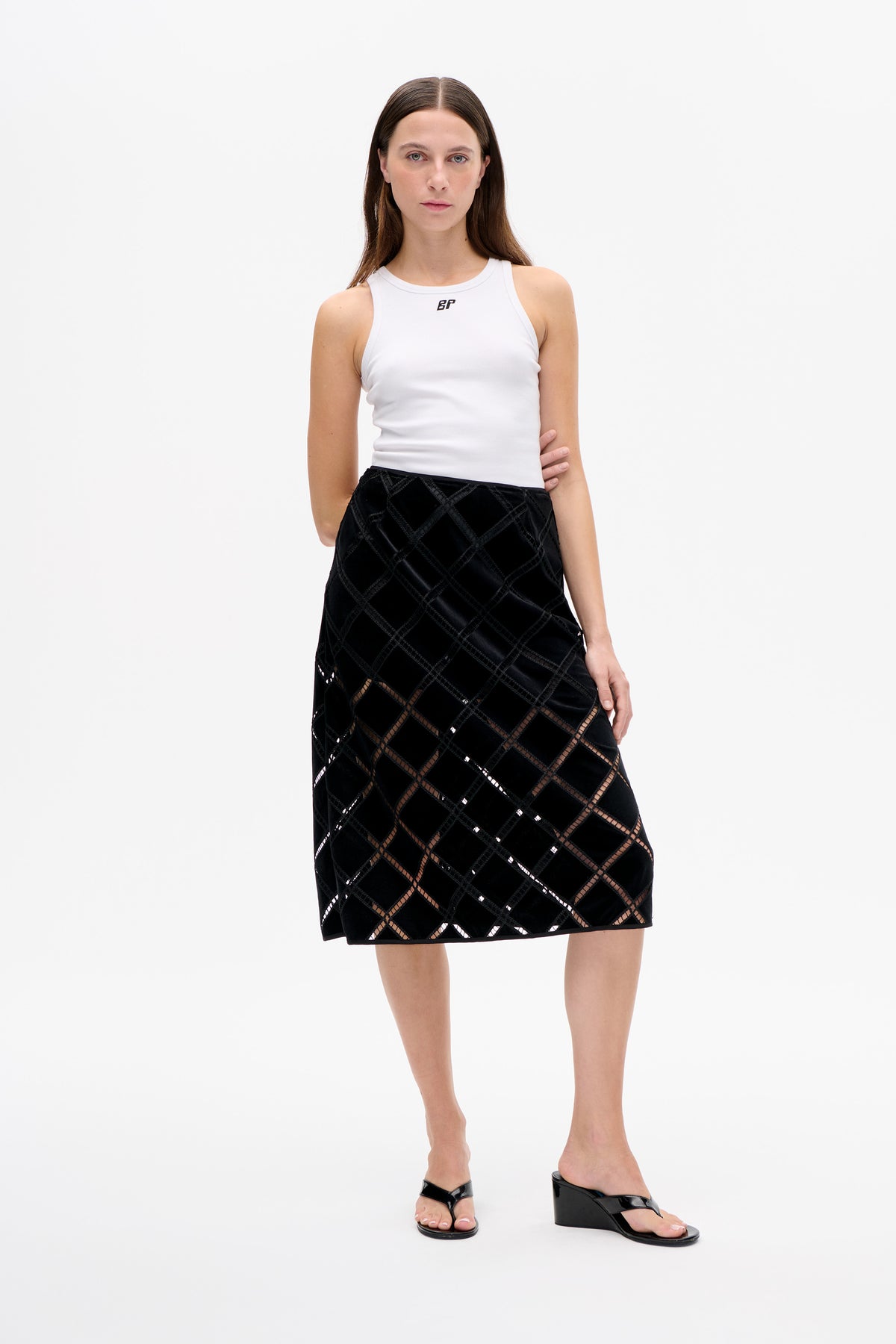 Model trägt weißes, geripptes, ärmelloses Top mit kleinem Brustlogo und schwarzen Midi-Rock mit geometrischen Cut-outs.