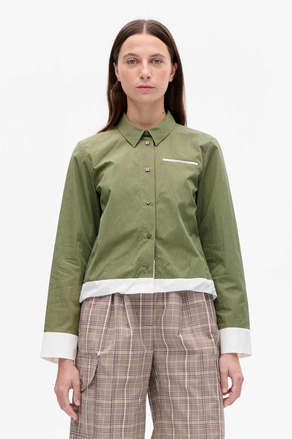 Front view of an olive-green button-up shirt with a pointed collar, white-trimmed chest pocket, contrast hem and cuffs, worn with beige plaid trousers.