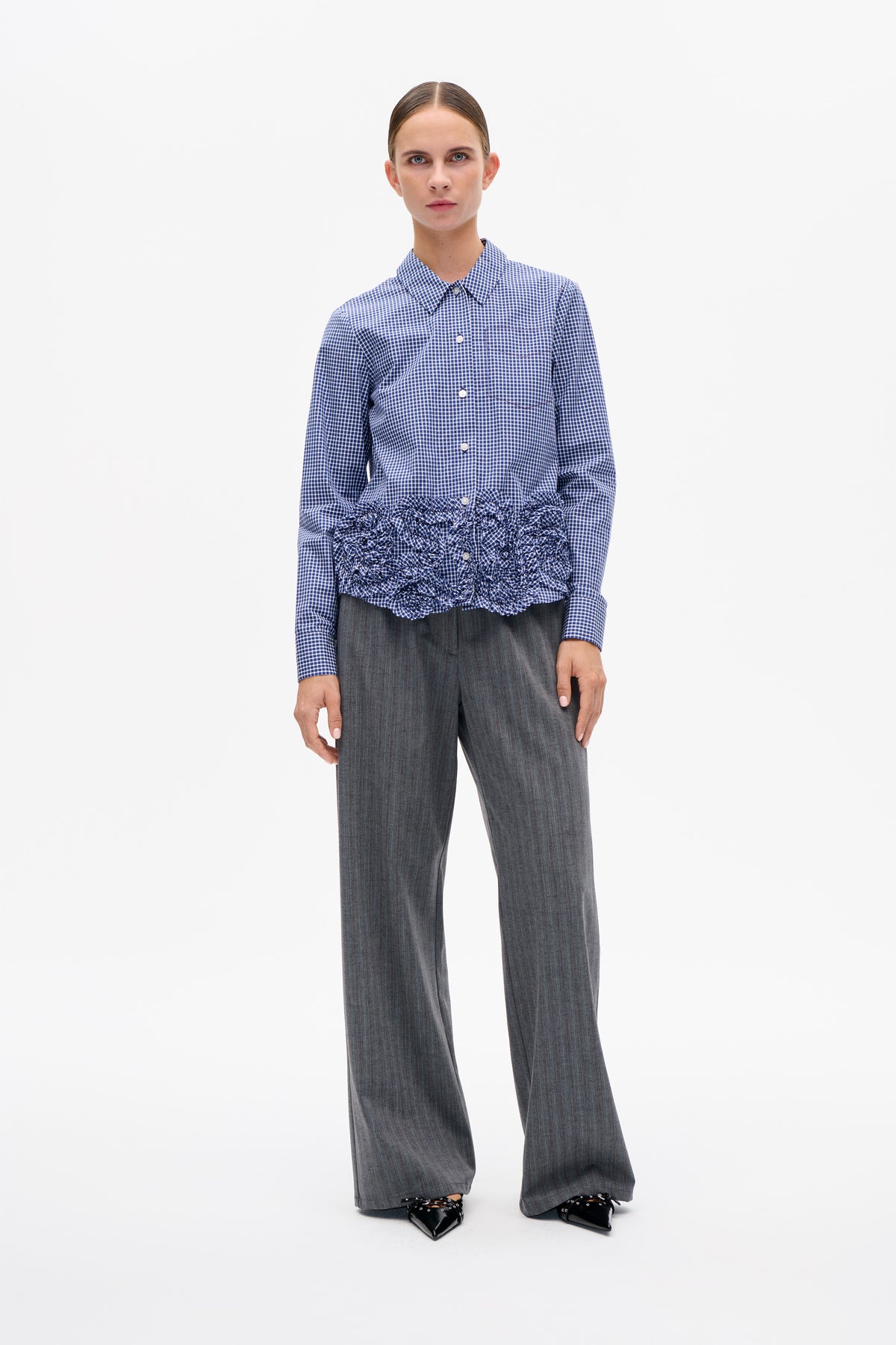 Vooraanzicht van een blauw-wit ruitjesblouse met knoopsluiting en een gerimpelde zoom, gecombineerd met een grijze, wijd uitlopende broek.