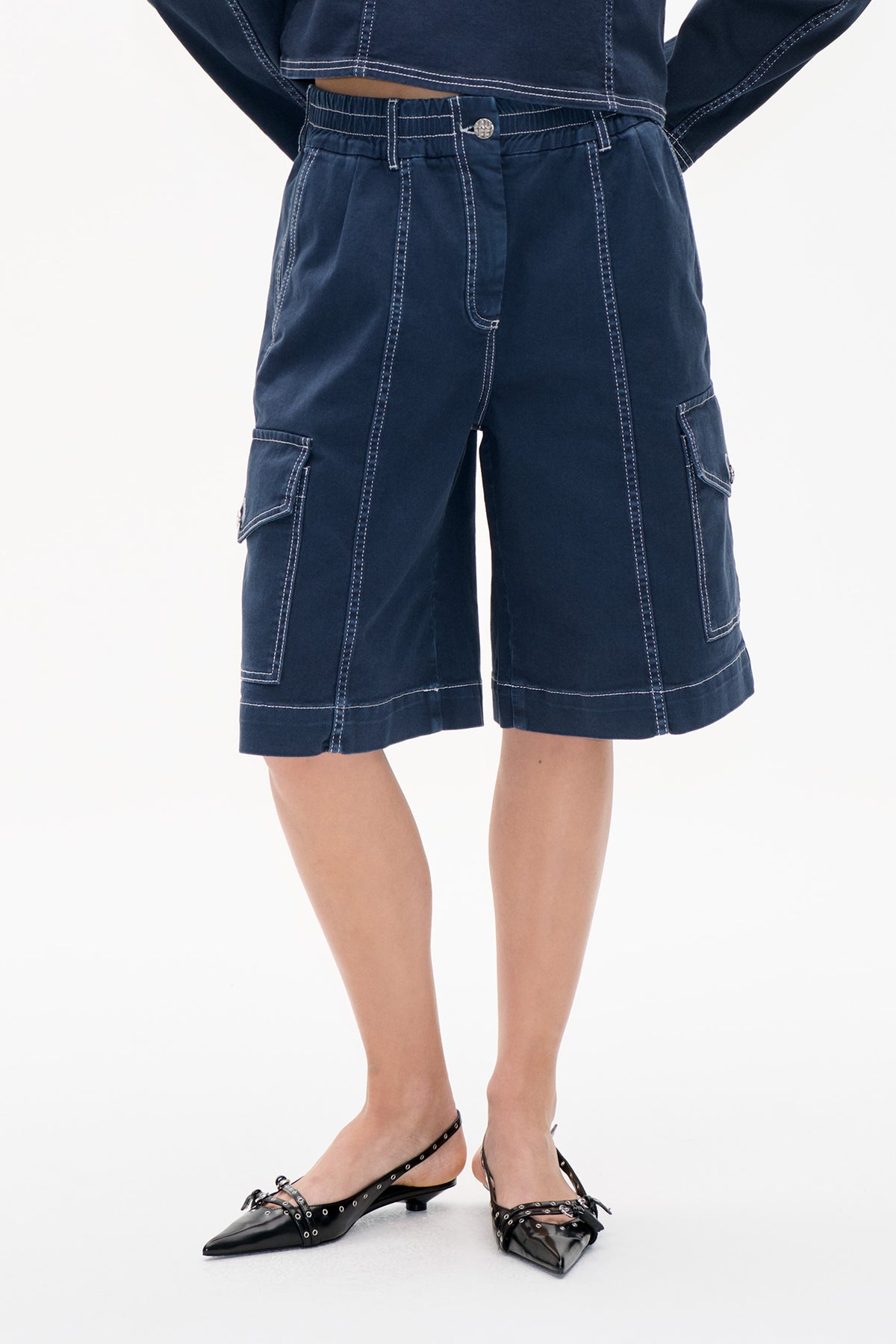 Frontdetail von dunkelindigofarbenen denim-Cargo-Shorts mit elastischem Bund, weißer Kontrastnaht und großen Seitentaschen.