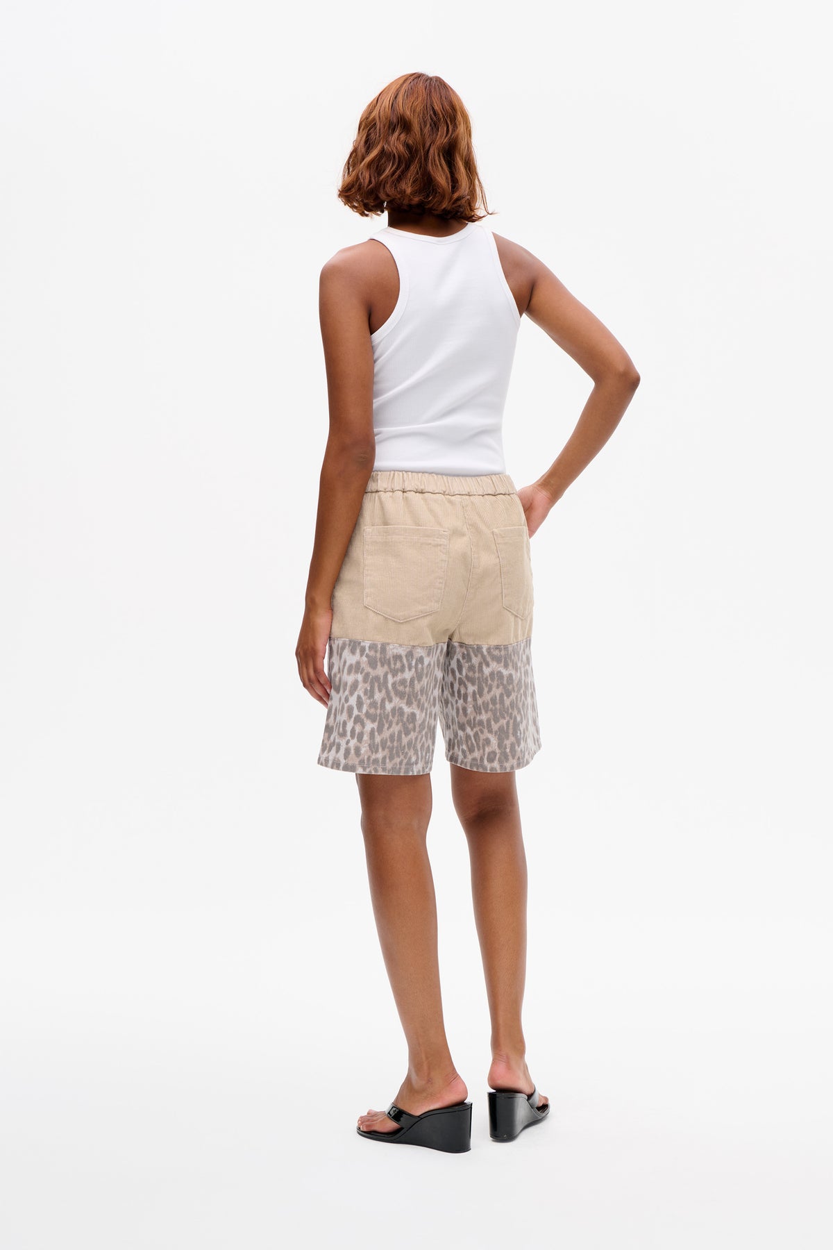 Back view of a model wearing a white ribbed tank top and beige shorts with a grey-brown animal print lower section and back pockets.