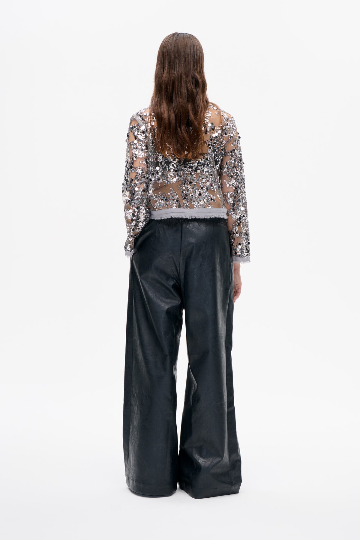 Back view of a sheer long-sleeved top covered in silver and black sequins, paired with black wide-leg trousers.