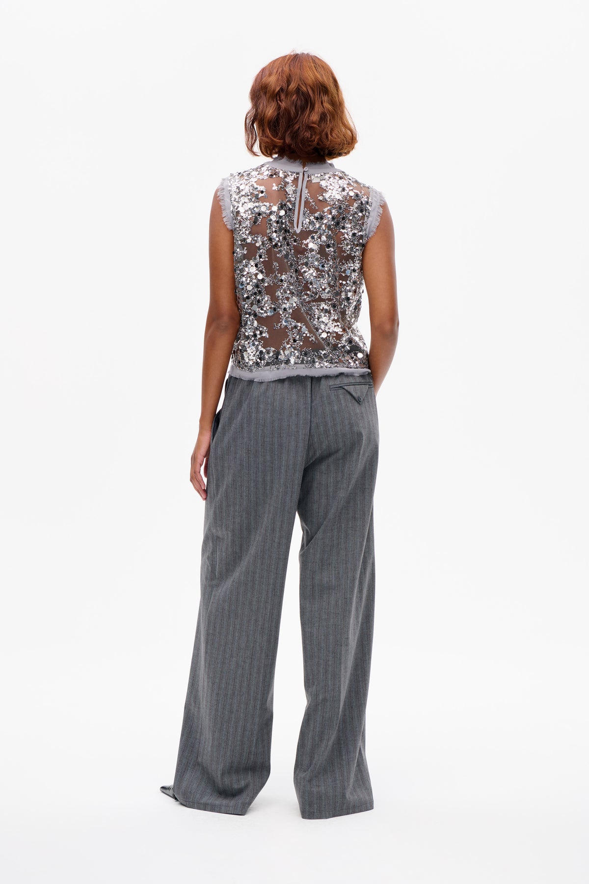 Vue de dos d'un top sans manches gris transparent, densément orné de sequins argentés et noirs, porté avec un pantalon gris à jambes larges.