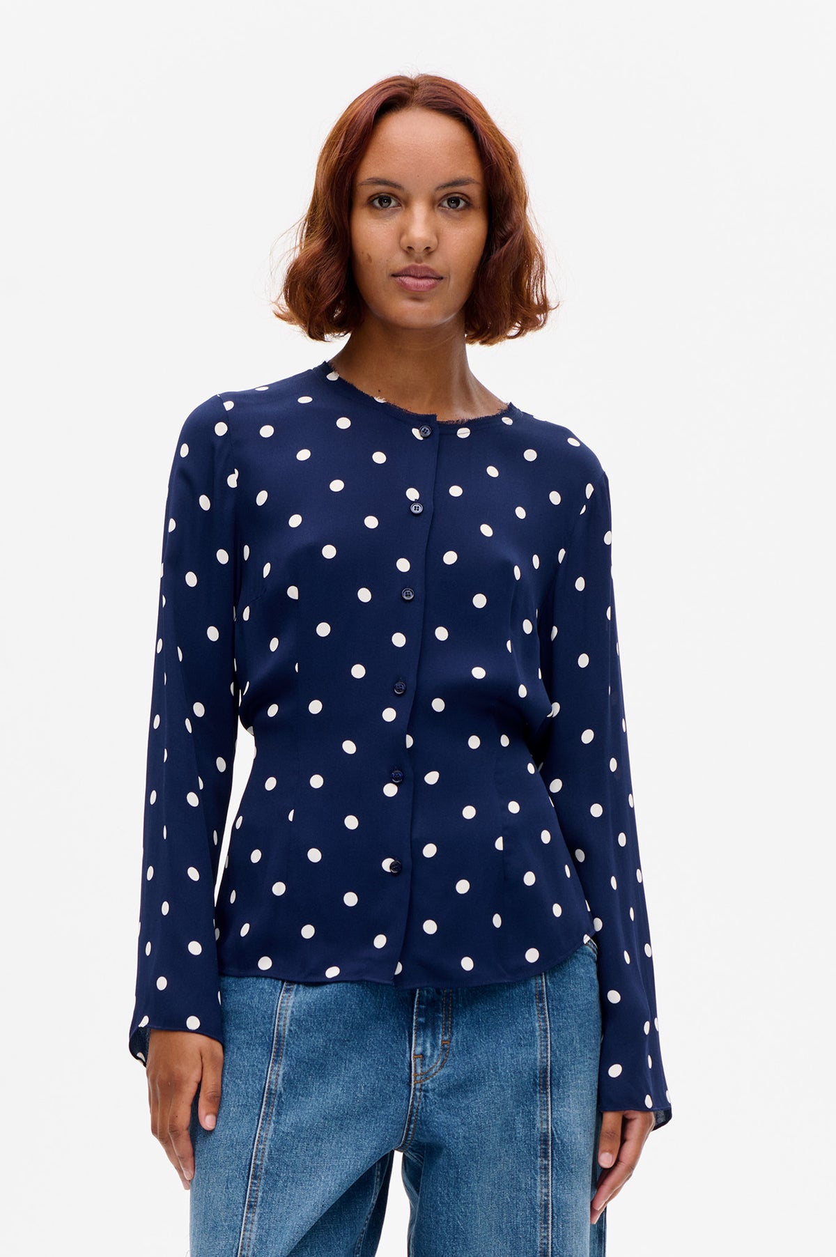 Front view of a navy long-sleeved button-front blouse with large white polka dots, worn with blue jeans.