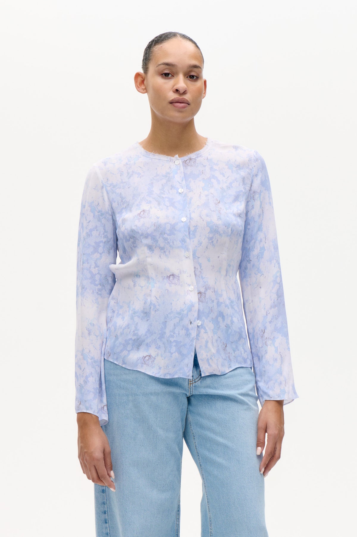 Front view of a model wearing a pale blue and lavender floral button-front blouse with a frayed neckline and light-wash jeans.