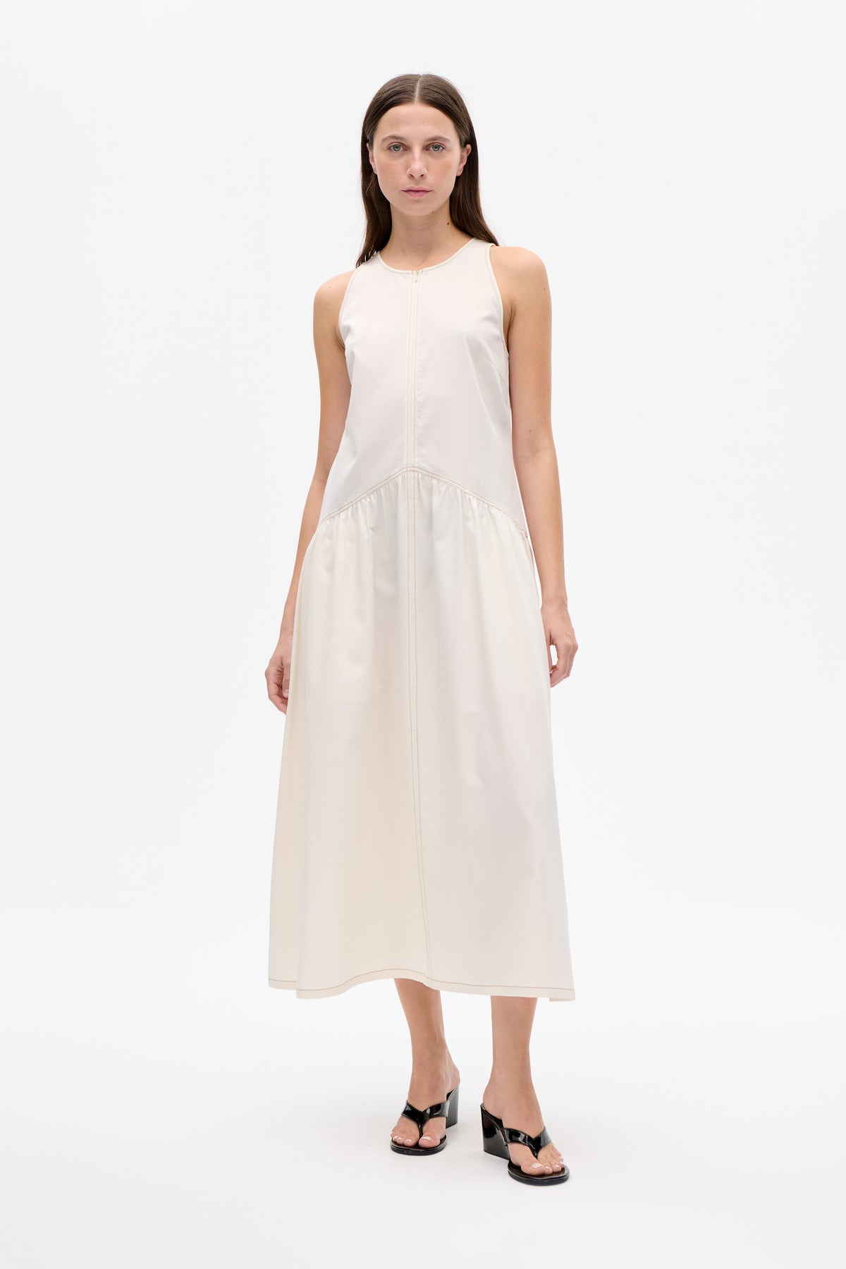 Model wearing an ivory sleeveless midi dress with a round neckline, front seam and gathered lower skirt.