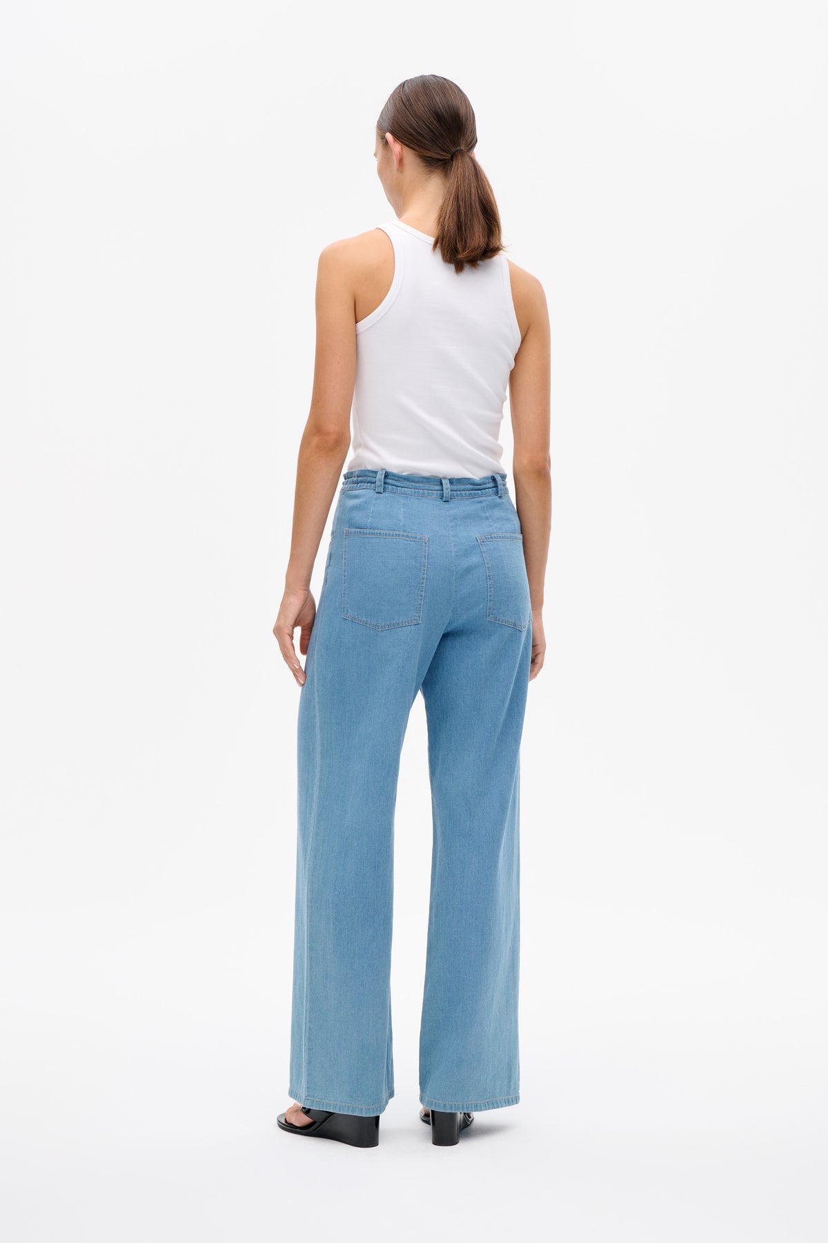 Rückenansicht eines Models mit weißem, geripptem Tanktop und hellblauen Jeans mit weitem Bein und zwei aufgesetzten Gesäßtaschen.