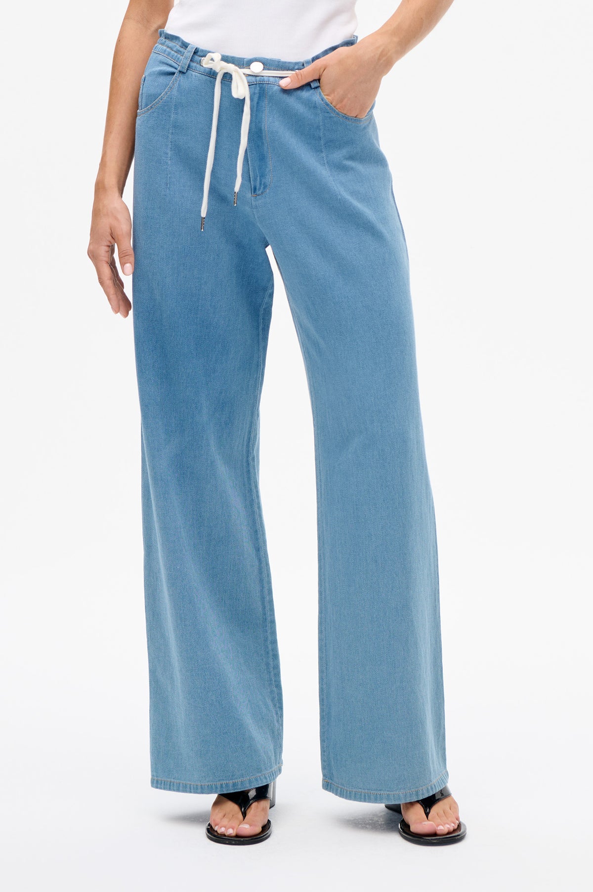 Detailansicht der Vorderseite einer weiten hellblauen denim-Hose mit weißem Kordelzug am Bund und Vordertaschen.