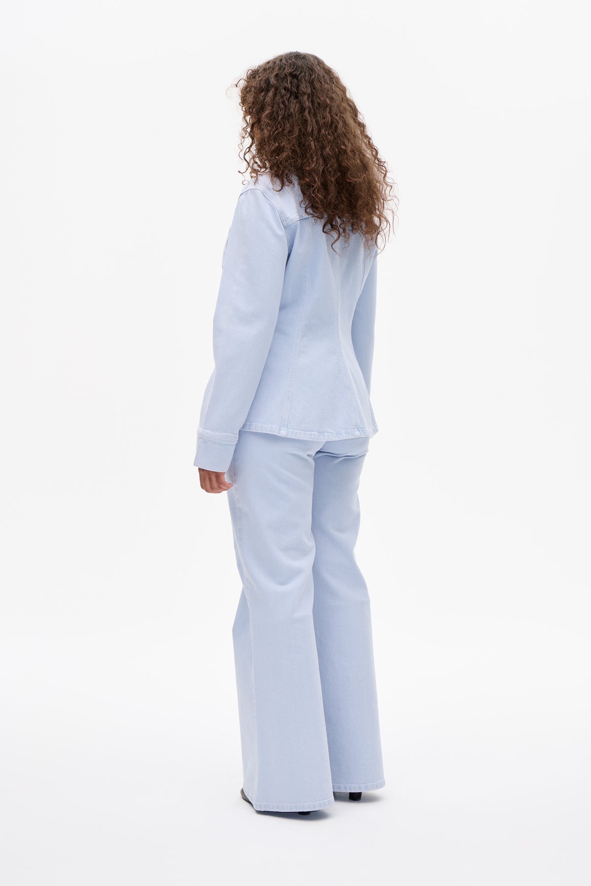 Back view of a model wearing a pale blue denim jacket with matching wide-leg jeans.
