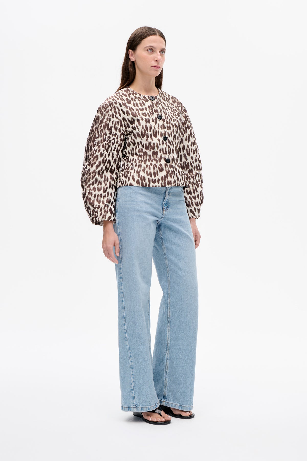 Model wearing a brown and cream animal-print button-front jacket with voluminous sleeves, light blue wide-leg jeans and black sandals.