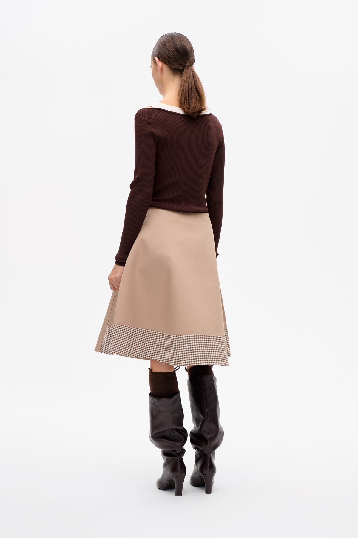Vue de dos d'un mannequin portant un haut côtelé à manches longues marron foncé et une jupe beige avec un ourlet vichy marron et blanc.