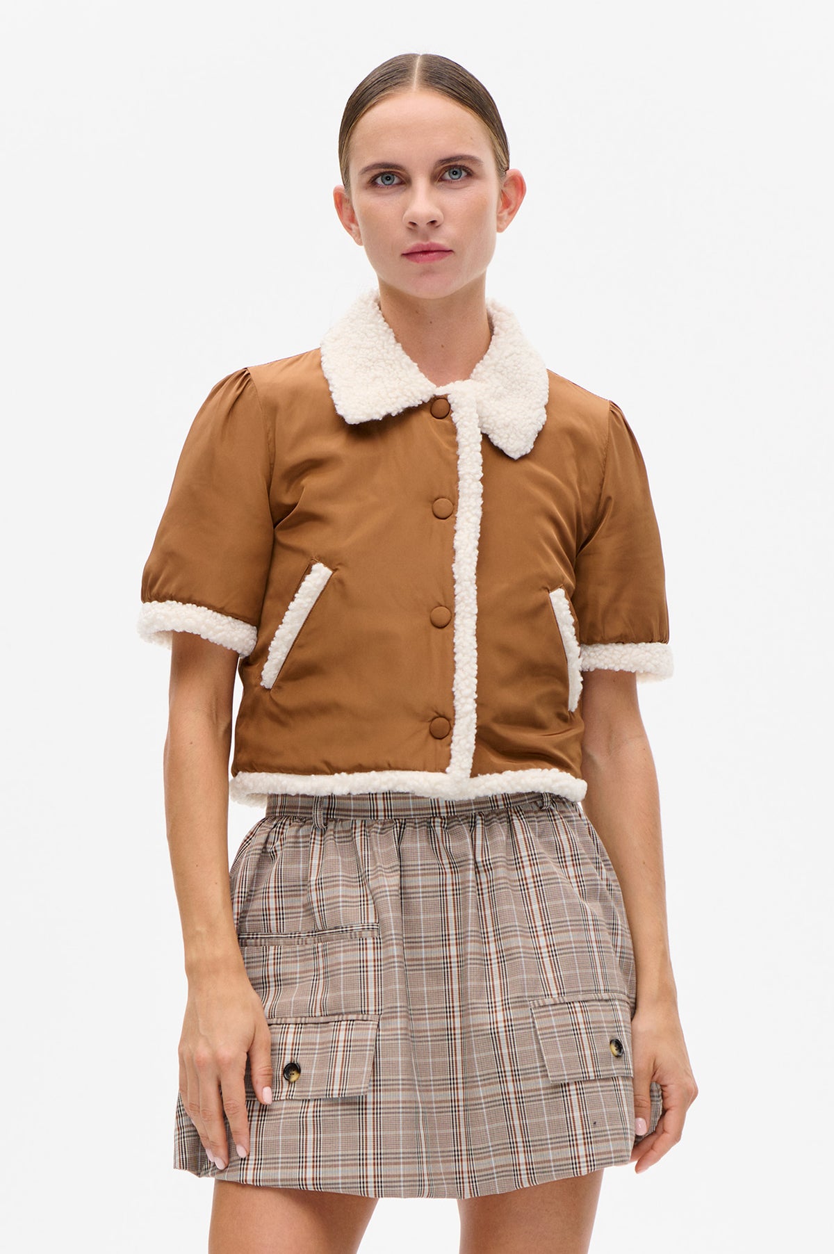 Front view of a caramel-brown short-sleeved jacket with cream textured trim and covered buttons, paired with a beige plaid skirt.